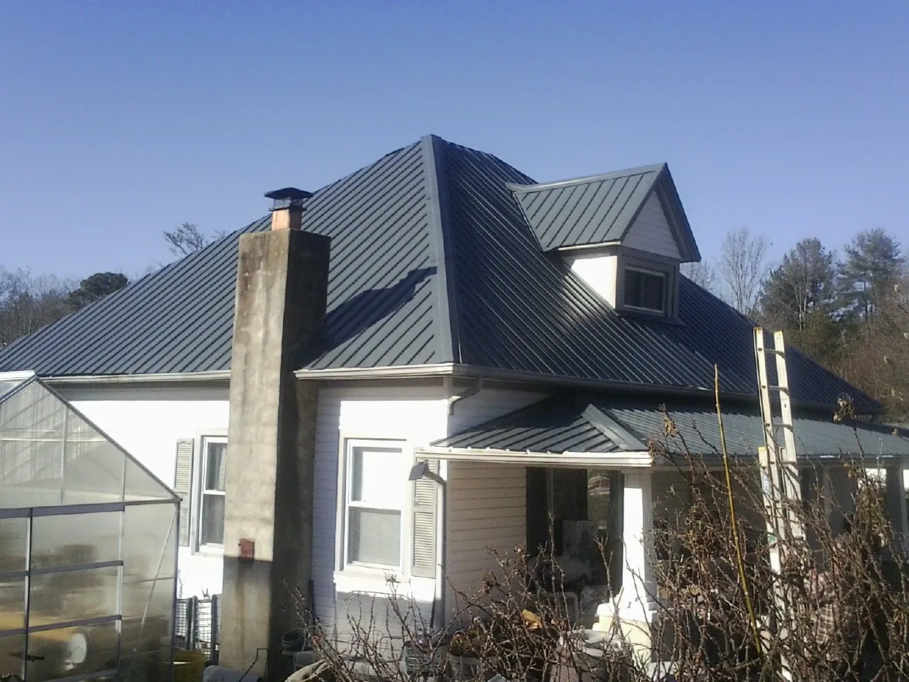 Dark blue standing seam metal roof on a white farmhouse with dormer — Slate & Tile Roof Repair by Roofing Brothers in Santa