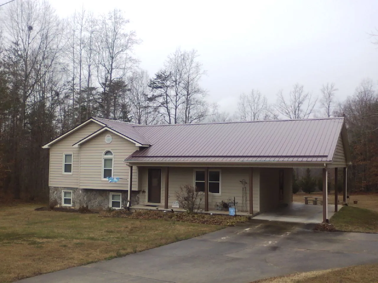 Burgundy metal roof on a tan split level home with an attached carport in Santa