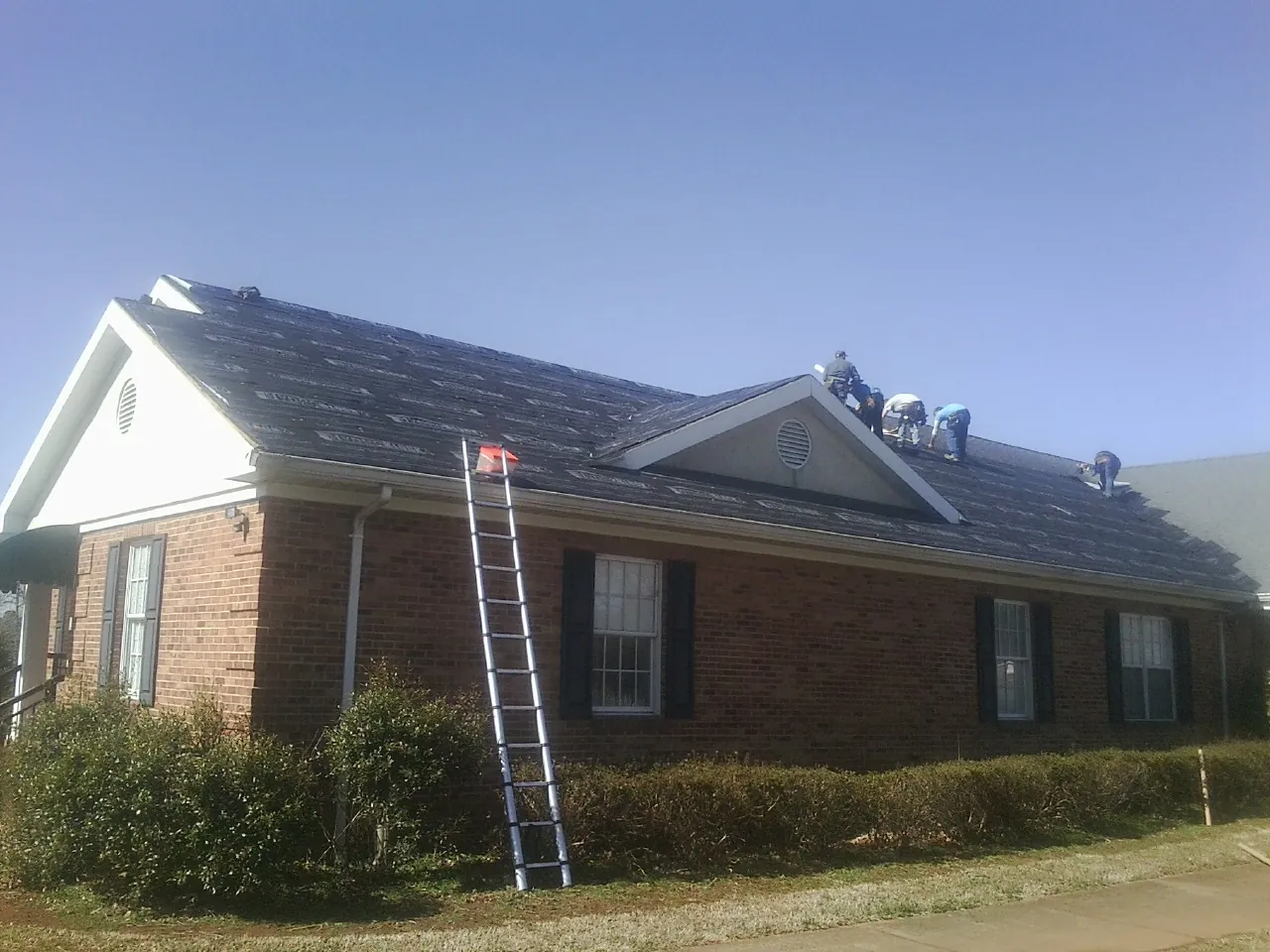 Crew tearing shingles off a brick ranch roof with a ladder set — Emergency Roof Repair work by our crew in Santa