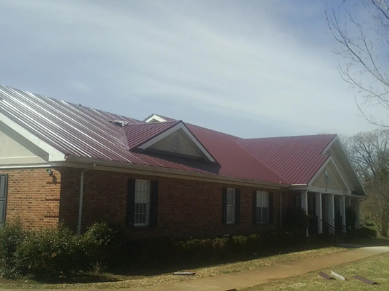 Red metal roof with gabled entries on a long brick building, from a Hail Damage Roof Repair job in Santa