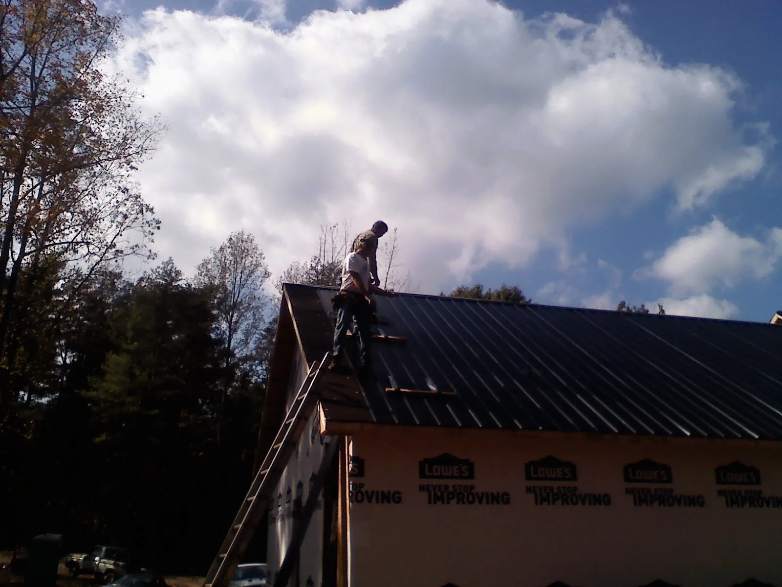 Roofer fastening dark metal panels high against a cloudy sky, from a Roof Inspection job in Santa