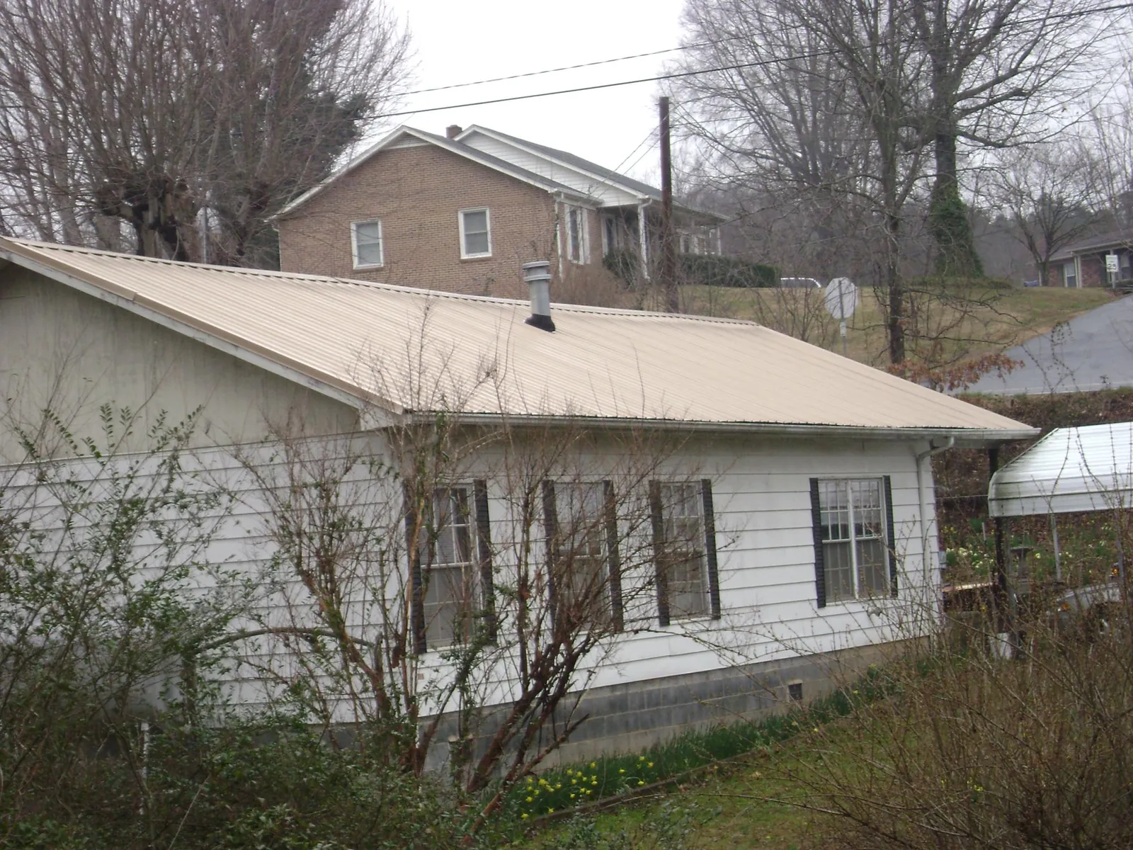 Tan metal roof on a white sided house set into a hillside — Commercial Roofing by Roofing Brothers in Santa