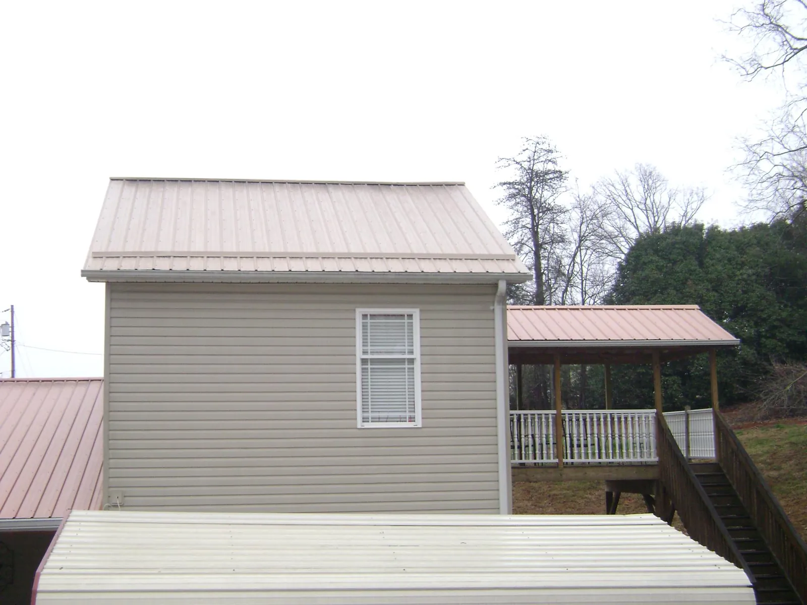 Tan metal roofs on a two story addition and attached porch, from a Roof Replacement job in Santa